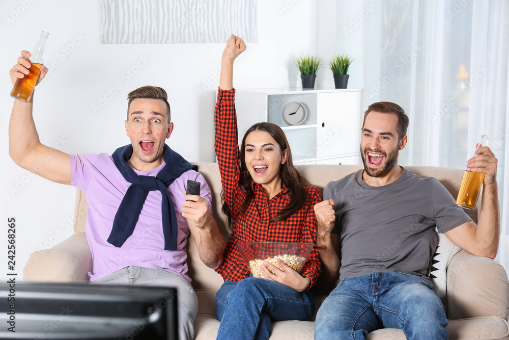 Wall mural Young friends watching TV on sofa at home