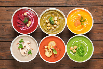 Various cream soups in bowls on wooden background, top view
