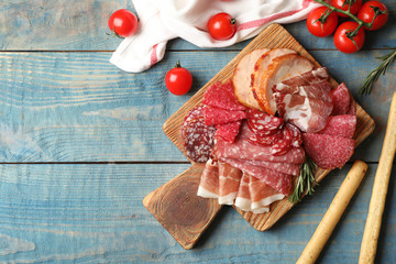 Cutting board with different sliced meat products on wooden background, flat lay. Space for text