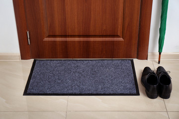 Welcome mat, male shoes and umbrella at door in hall