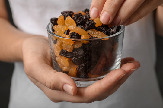 Woman holding glass with raisins on black background, closeup