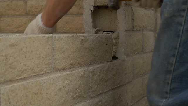 A construction worker chiseling brick out of a wall