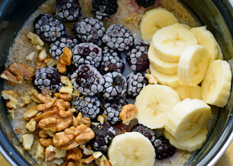 Delicious and healthy breakfast with oatmeal, nuts and berries. Walnuts, bananas and blackberries for cooking porridge. Healthy food, vegetarianism. The cooking process, top view.