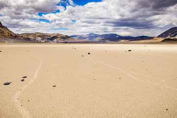 Moving rocks and their tracks at the Racetrack Playa; mountains and clouds scenery in the background; Death Valley National Park, California