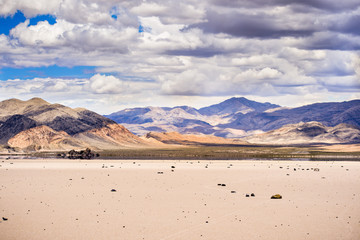 Moving rocks scattered around the surface of the Racetrack Playa; mountains and clouds scenery in the background; Death Valley National Park, California