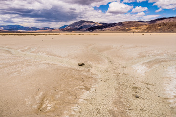 Fototapeta na wymiar Signs of streams of running water at the Racetrack Playa; mountains and clouds scenery in the background; Death Valley National Park, California