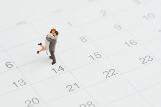 Miniature people figure lovely couple holding each other standing on 14th Feb calendar as wedding anniversary or Valentine's day celebration