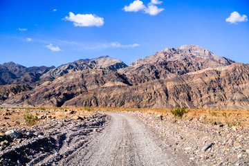 Driving on an unpaved road towards the entrance to Titus Canyon, Death Valley National Park; steep mountains in the background; California