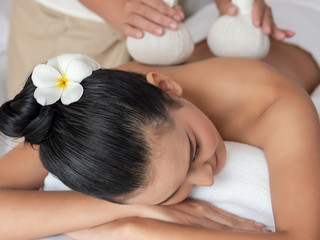 Obraz na płótnie Canvas Beautiful young asian woman lying on the bed having a massage with herbal compresses in a spa. Thai massage for health. Select focus face women