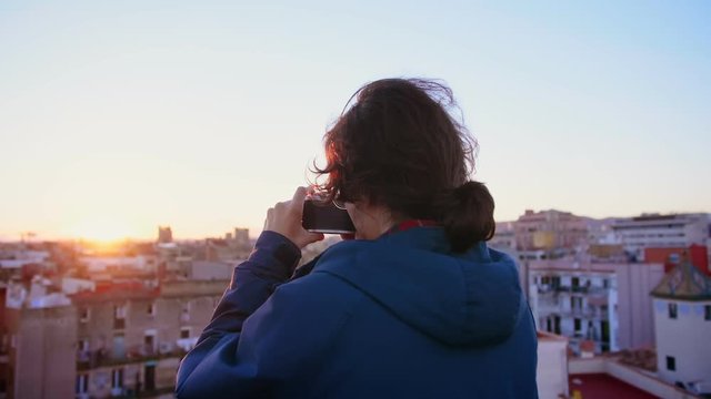 Young hipster student in Erasmus new in city learning photography as a hobby and taking an analog photo or picture by lomo old film camera of view of rooftop during sunset or sunrise in Europe town