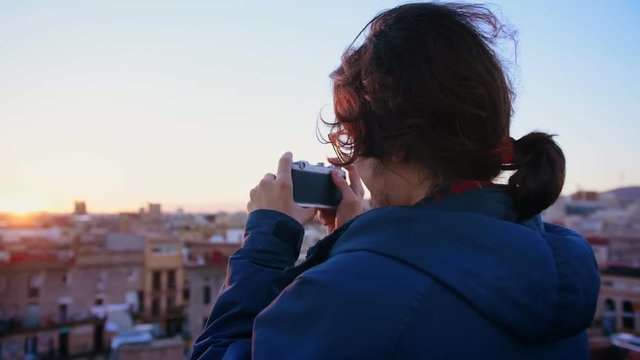 Young hipster student in Erasmus new in city learning photography as a hobby and taking an analog photo or picture by lomo old film camera of view of rooftop during sunset or sunrise in Europe town
