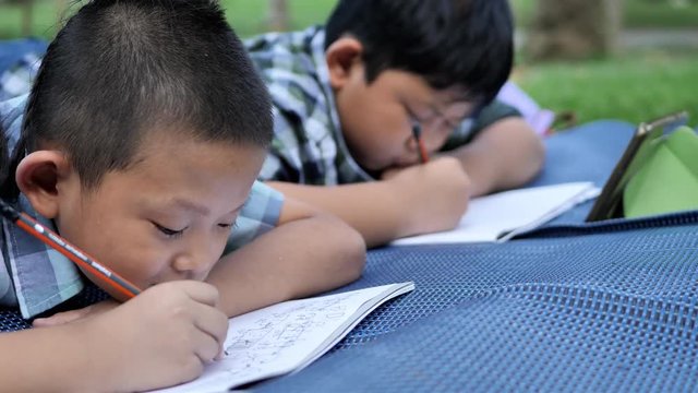 Two Asian boys drawing on mat in a book at park...concept education