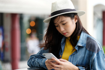 Young asian woman using phone standing in front of cafe in the city outdoors background, people working outdoors with technology, lifestyle