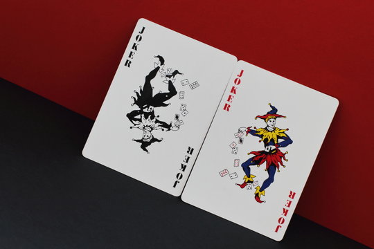 The game of imagination. Card allegory is red and black as symbol of opposites and contradictions in world. Red and black joker on contrasting red and black background.