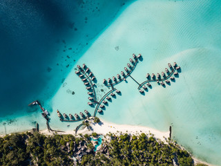 Luxury overwater villas with coconut palm trees, blue lagoon, white sandy beach at Bora Bora...
