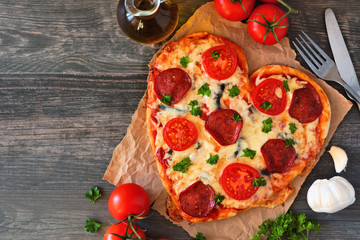 Heart shaped pizza for Valentines Day over a rustic wood background. Top view, side border. Table...