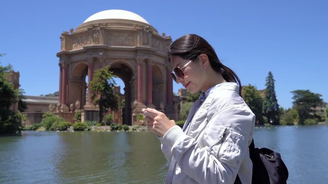 happy asian girl traveler visiting palace of fine arts taking photo by cellphone camera app. woman tourist using smart phone take pictures old history building in san francisco california usa.