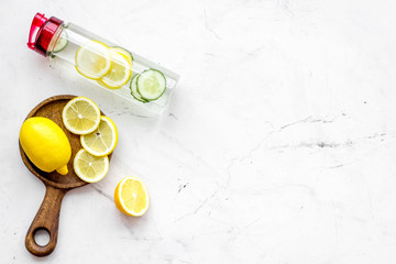 Detox infused water with slices of lemon and cucumber in bottle on white stone background top view copy space