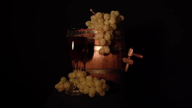 Slowly rotating wine barrel with grape and glass of wine.