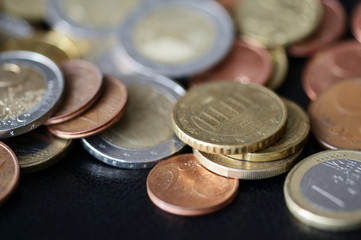 A pile of euro coins scattered on a dark surface close up