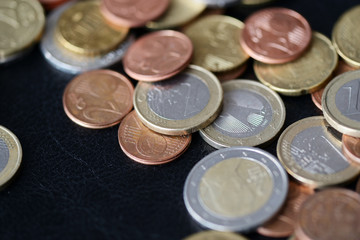 A pile of euro coins scattered on a dark surface close up