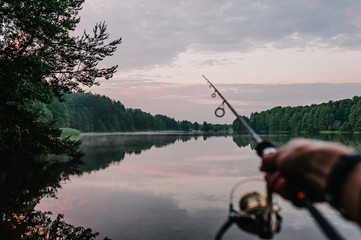 Fisherman with rod, spinning reel on the river bank. Sunrise. Fishing for pike, perch, carp. Fog against the backdrop of lake. background Misty morning. wild nature. The concept of a rural getaway.