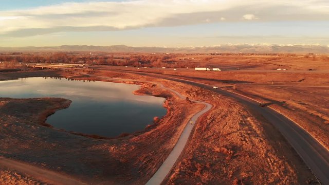 Electric Skateboarding on Curvy Path with Lake, Highway, and Mountains at Golden Hour Aerial Following View