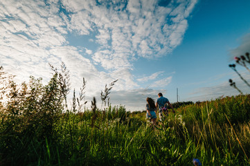 Rear view of a romantic man and woman walking on field grass, nature enjoying stunning sunset. Concept of lovely family holding hands. Young couple running and looking away.