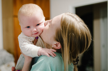 Happy mother and daughter. Mom holds on hands and kissing little baby girl, concept happy family, lifestyle. newborn. Photo shoot 4-5 months.