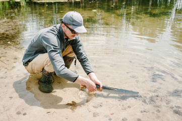 The fisherman releases a large fish under the water, a big pike in the pond. Sports fishing. Man hold a pike in lake on a background nature. Fishing background. Good catch. Trophy fish. angler.