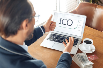 Business Lifestyle. Trader sitting at cafe with coffee and laptop using ico looking at chart thumb...