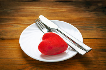 Red Plush Heart with Fork and Knife in Finished the Meal Position on a White Plate. Wooden Background. Minimalist Healthcare, Breakup Symbol. Card, Message, Banner Design.