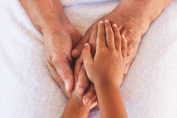 Hands of asian child girl holding elderly grandparent hands wrinkled skin with feeling care and love