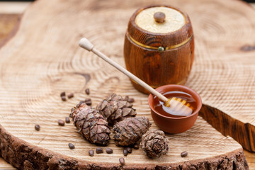 Barrel with honey and a spoon on a wooden saw and pine nuts and cones. Textured wood products.