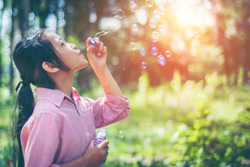 Asian girl wearing a pink shirt, being within the Park. She is currently blowing soap bubbles with...