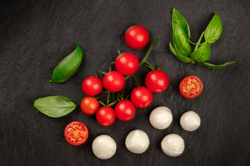 Naklejka na ściany i meble An overhead photo of Mozzarella cheese, cherry tomatoes and fresh basil leaves on a black background, Italian cuisine ingredients with copyspace