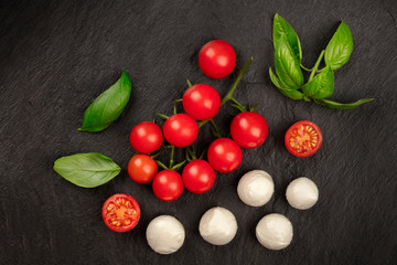 An overhead photo of Mozzarella cheese, cherry tomatoes and fresh basil leaves on a black background, Italian cuisine ingredients with copyspace