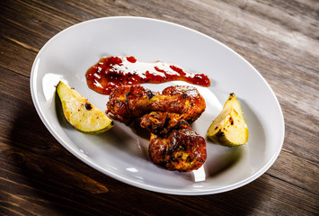 Grilled chicken drumsticks with pear on wooden background