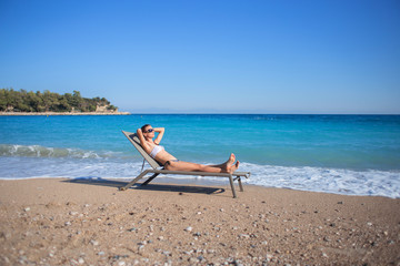 The slender girl lies on a sun bed at a sea edge against the background of the Mediterranean Sea.