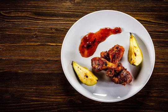 Grilled chicken drumsticks with pear on wooden background