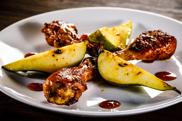 Grilled chicken drumsticks with pear on wooden background