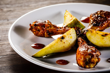 Grilled chicken drumsticks with pear on wooden background