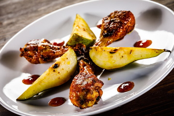 Grilled chicken drumsticks with pear on wooden background