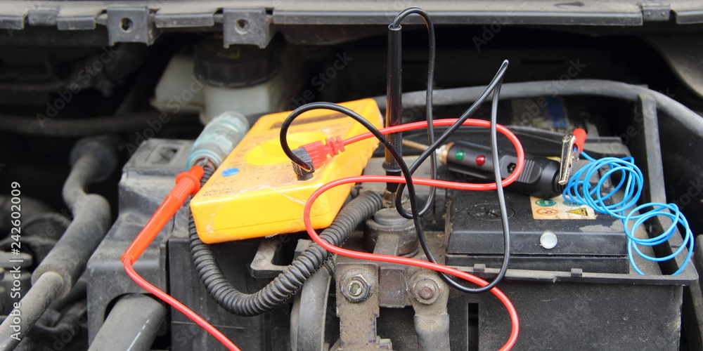 Poster Close up yellow tester digital multimeter with wires and probe diagnostic lamp on old black car battery accumulator - repair of vehicle electrical equipment