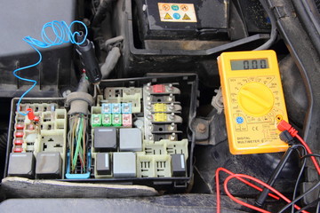 Close up yellow tester digital multimeter and probe diagnostic lamp on car fuse block - repair of vehicle electrical equipment
