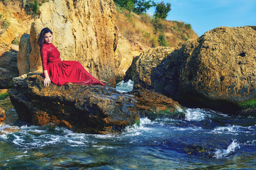 a young girl on the sea coast, a girl in a red dress resting sitting on the rocks