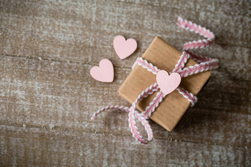 Mit Liebe schenken - Kleines Geschenk mit rosafarbenen Band und Herz auf Holz