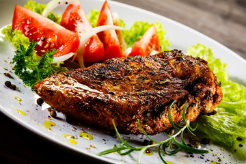 Grilled chicken fillet and vegetables on wooden background