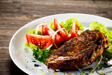 Grilled chicken fillet and vegetables on wooden background