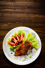 Grilled chicken fillet and vegetables on wooden background